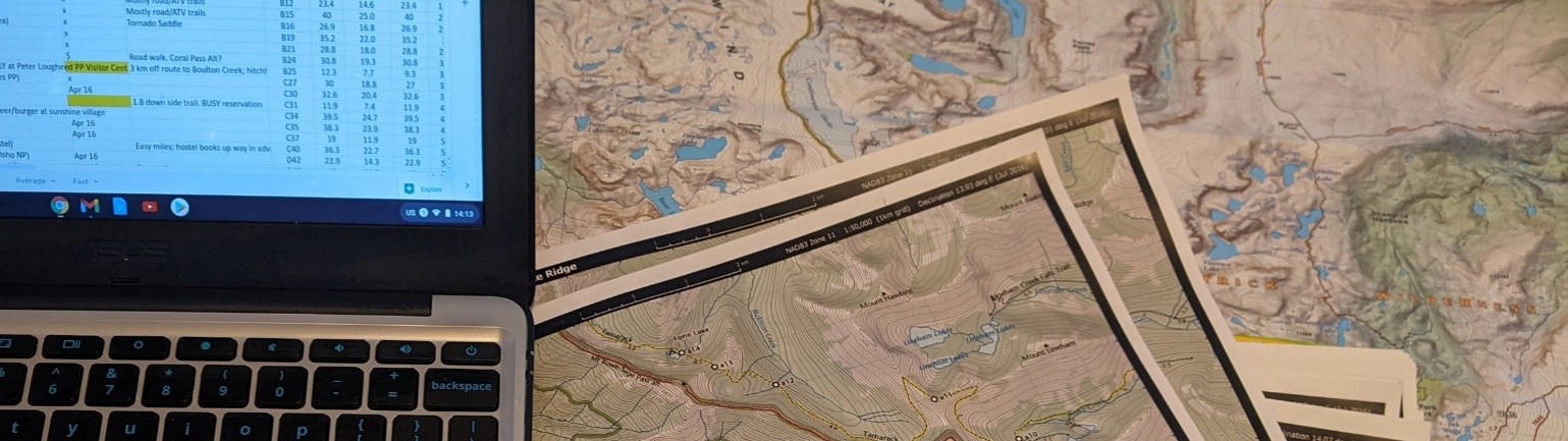 a laptop with a spreadsheet open and maps around it